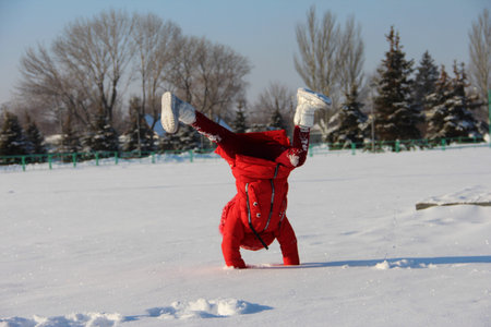 handstand in the snow, a child doing sports in the snow, a girl in a red jacket and a red hat with...