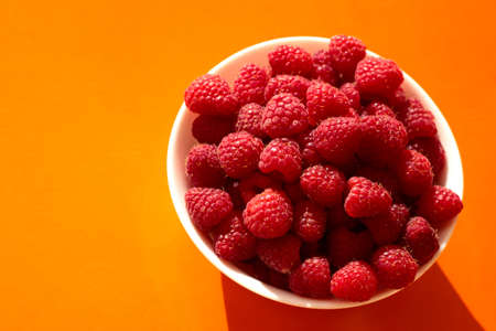 Raspberry berries in a white plate on an orange background.の写真素材