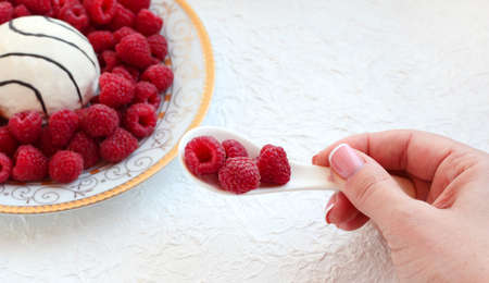 In the hand of a spoon with raspberries on a white background.の写真素材