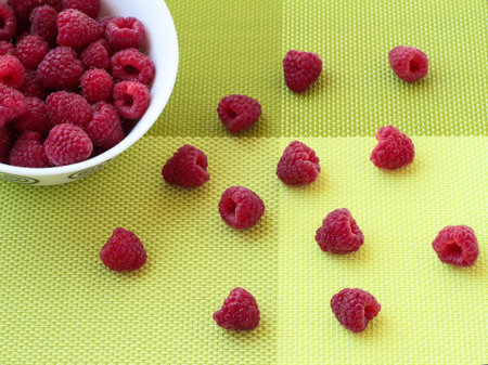 Ripe raspberries in a ceramic plate on a green background. Scattered berries.