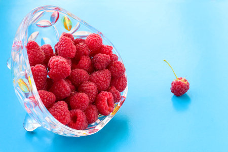 Ripe raspberries on a blue background in a crystal plate.