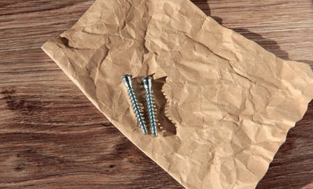 Self-tapping screws on crumpled paper and wooden background.の写真素材