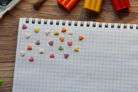 Notepad with sweet hearts on a wooden background with paints, plasticine and brushes. Hobbies and...