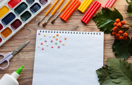 Notepad with sweet hearts on a wooden background with paints, plasticine and brushes. Hobbies and...