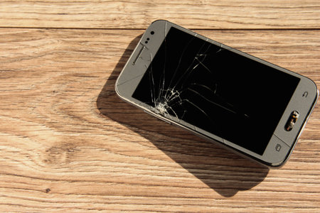 Broken phone on a wooden background. Cracks on the smartphone.