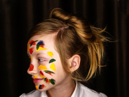 A girl stained with paint holds colored pencils.
