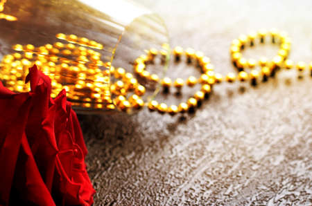 A glass with gold beads and a rose on a dark background.の写真素材