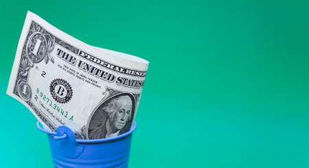 One dollar in a blue bucket on a green background.の写真素材