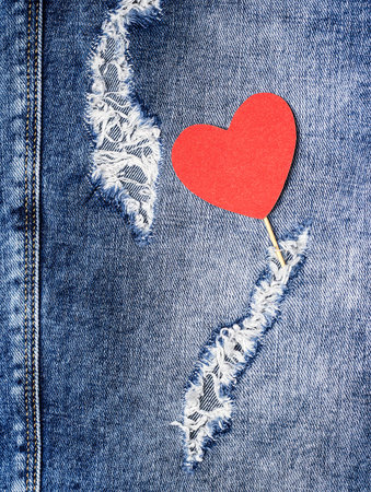 Red heart on a stick on a background of torn jeans.