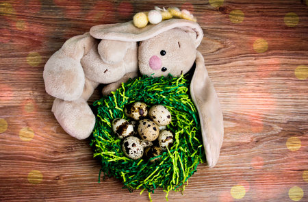 Plush bunny near the nest with eggs. Rabbit on a wooden background.