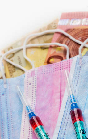 Medical syringes with a dose of medicine on masks and euro banknotes.の写真素材