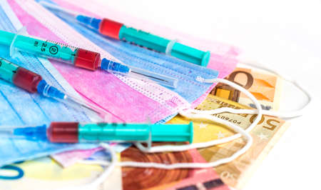 Medical syringes with a dose of medicine on masks and euro banknotes.の写真素材