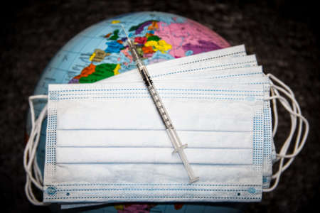 Medical syringe on masks on the globe.の写真素材
