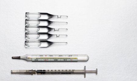 Ampoules with a medicine, a medical syringe and a thermometer on a light background.