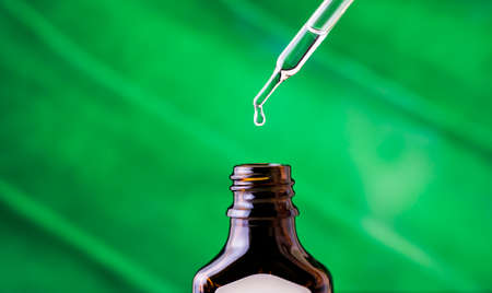 A drop of oil drips into a jar on a green background.の写真素材