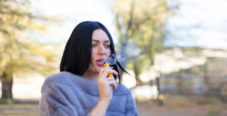 The girl smokes an electronic cigarette in the fresh air.の写真素材