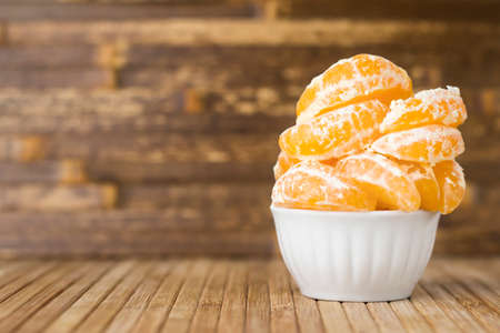 Tangerine slices in a white bowl on a wooden table.の写真素材