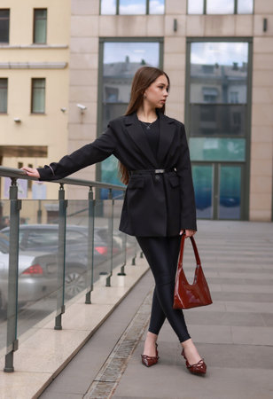 A girl in black clothes, burgundy patent leather shoes with a patent leather bag against the background of city shop windows.の写真素材