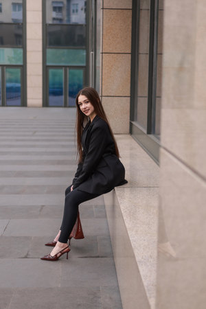 A beautiful girl in a black jacket and leggings against the backdrop of city streets.の写真素材
