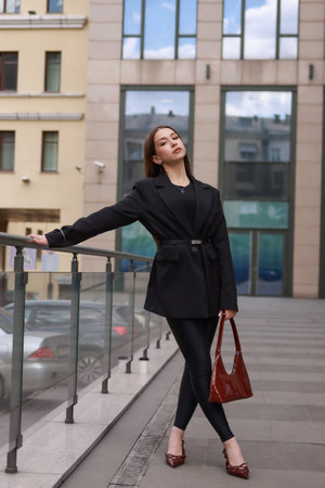 A girl in black clothes, burgundy patent leather shoes with a patent leather bag against the background of city shop windows.の写真素材
