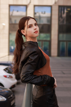 A stylish girl near a car dealership in a leather jacket and leather skirt.の写真素材