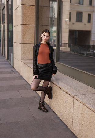 A girl with freckles in a leather skirt near a skyscraper.の写真素材