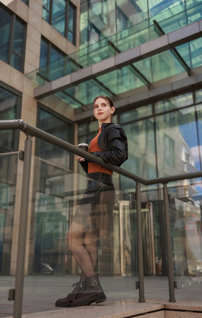 Girl with hot coffee against the background of a modern city building.の写真素材