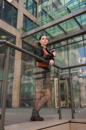 Girl with hot coffee against the background of a modern city building.の写真素材
