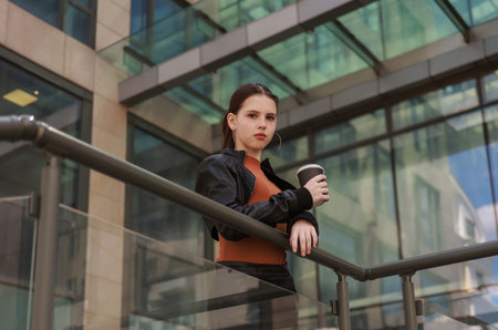 Girl with hot coffee against the background of a modern city building.の写真素材