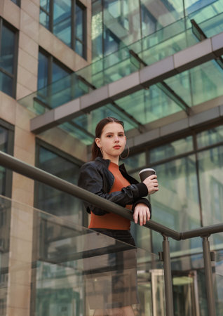 Girl with hot coffee against the background of a modern city building.の写真素材