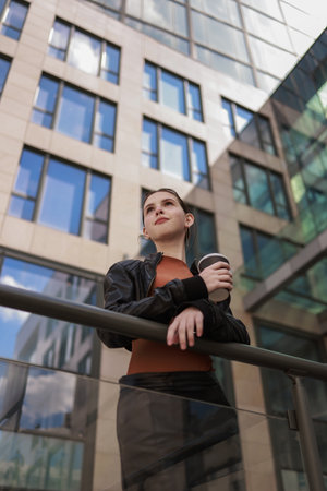 Girl with hot coffee against the background of a modern city building.の写真素材