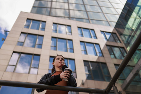 Girl with hot coffee against the background of a modern city building.の写真素材