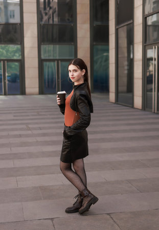 Girl with hot coffee against the background of a modern city building.の写真素材