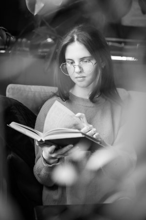 The girl is reading a book while sitting on the sofa.の写真素材