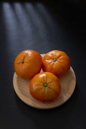 Three clementine tangerines in wooden bowl on black backgroundの写真素材