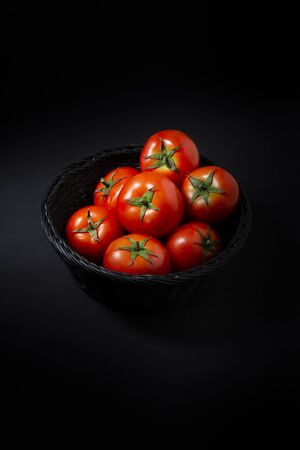 Tomatoes in black basket, all on black backgroundの写真素材