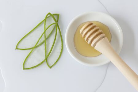aloe vera leaves chopped into thin slices, bowl with honey and honey-pot grinder with white backgroundの写真素材