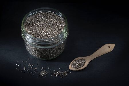 Glass jar with chia seeds, a wooden spoon, on a black backgroundの写真素材