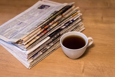 selective focus of the cup of tea stacking newspapers folded place on wooden tableの写真素材