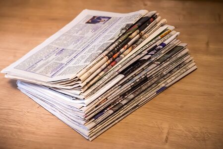 Newspapers folded and stacked on the table with wood background. Closeup newspaper and selective focus image. Time to read concept.の写真素材
