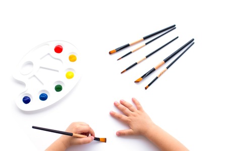 On a white isolated background palette with primary colors paints, children's hands and a set of brushes for drawing.の写真素材