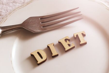 Empty white plate and fork, diet inscription in wooden letters, healthの写真素材