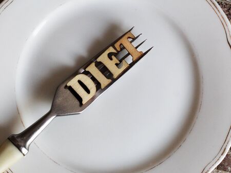 Empty white plate and fork, diet inscription in wooden letters, healthの写真素材