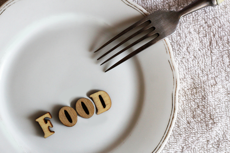 Empty white plate and fork, food inscription in wooden letters, healthの写真素材