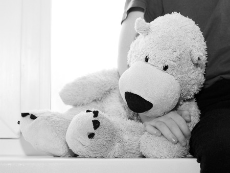 bear sad toy sitting on the window, child's handの写真素材
