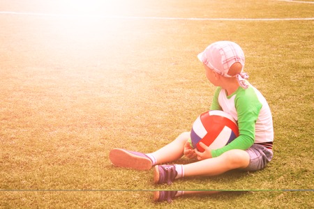 Uncertain baby boy sitting next to soccer ball at football field. Football training concept. Toned.の写真素材