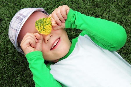 A little boy lies on the grass and closes his eyes with yellow leaves. Portrait.の写真素材