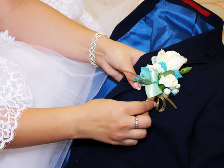 The bride's hand puts on a boutonniere flower on the groom's jacket.