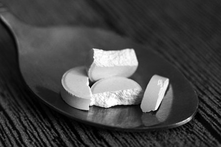 White tablets in a spoon on a wooden table so close