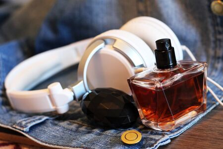 Bottle of perfume and headphones on the jeans, wooden background, brown colorの写真素材